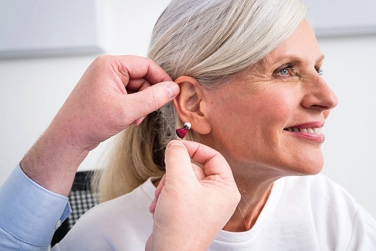 Ältere Frau bekommt ein modernes Hörgerät eingesetzt, Hörakustiker berät zur Hörhilfe.