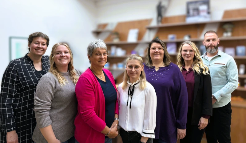 Eine Gruppe von sieben Mitarbeitenden steht gemeinsam in einem modernen Büro vor Bücherregalen.